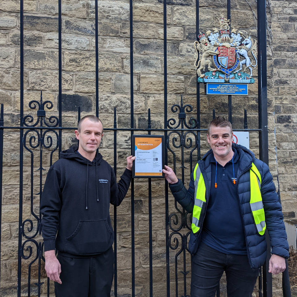 Mark and Richard stand in front of the AW Hainsworth gates with the ISO 45001 health and safety certificate